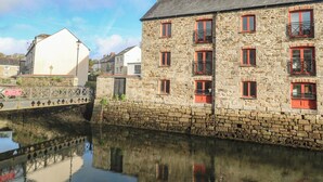 Ein Steinhaus mit zahlreichen Fenstern und Balkonen, einer Brücke und einem ruhigen Gewässer, das das Gebäude widerspiegelt.