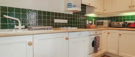 Una cocina con armarios blancos, microondas, tostadora y un reloj en la pared.