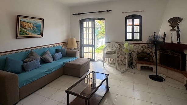 Uma sala de estar com sofá, mesa de centro, quadro, lareira e janela.