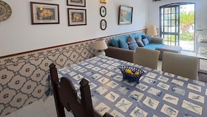 Uma área de refeições com uma mesa posta para quatro pessoas, um sofá e uma parede com quadros e uma luminária fixada.
