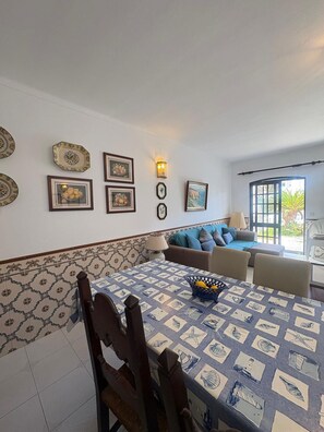 A dining area with a table set for four, a sofa, and a wall with framed pictures and a wall-mounted light. - Villa Praia (Altura)