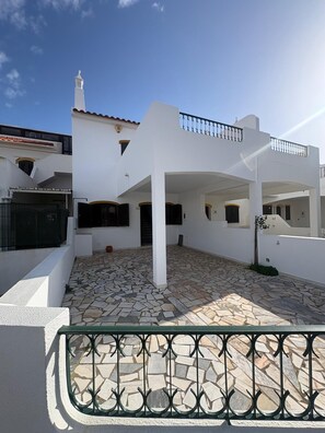 A white building with a tiled courtyard, a balcony, and a stone floor. - Villa Praia (Altura)