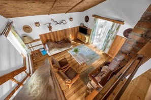 A wooden interior with a loft bed, a dining table, and a fireplace.