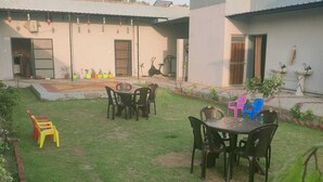 Un patio con una mesa y sillas para comer, un pequeño espacio de juegos con juguetes, y un edificio con una puerta y ventanas.