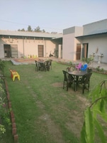Um pátio com uma mesa de jantar e cadeiras, uma pequena área de recreação com brinquedos e um edifício com porta e janelas.