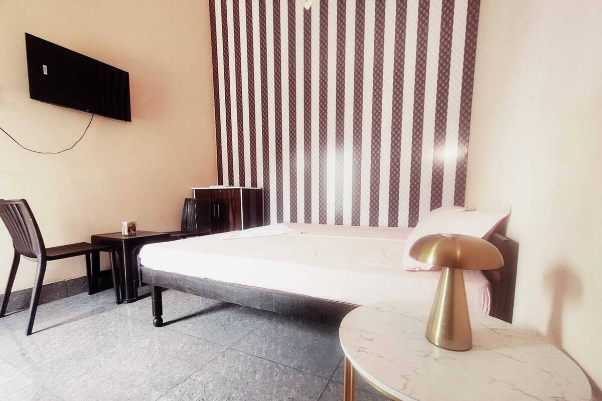 Ein Hotelzimmer mit Bett, Schreibtisch, Stuhl, kleinem Tisch, Wandfernseher und einem gemusterten Vorhang.