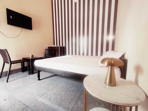 Habitación de hotel con cama, escritorio, silla, mesita pequeña, televisión montada en la pared y cortina estampada.