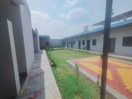 Um pátio com calçada pavimentada, área gramada e um edifício com telhado plano e várias janelas.