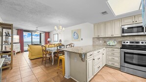 A modern kitchen with a central island, built-in appliances, and a dining area with yellow chairs. - 2BR Beachfront retreat in Orange Beach w/ pools & tennis (Orange Beach)