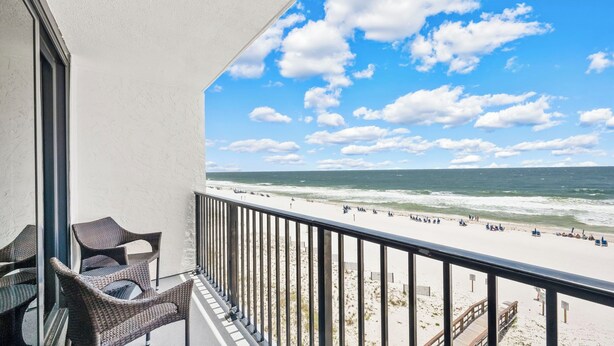 A balcony with wicker furniture overlooking a beach with a clear sky. - 2BR Beachfront retreat in Orange Beach w/ pools & tennis (Orange Beach)