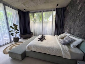 A modern bedroom with a large bed, a stone accent wall, and a view through sheer curtains. - Villa Karma | 2BR pool villa in Seseh (Mengwi)