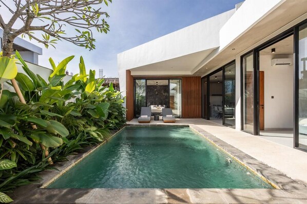 A modern house with a swimming pool, a patio with seating, and a large glass door leading to a living area. - Villa Karma | 2BR pool villa in Seseh (Mengwi)