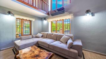 Un salon comprenant un canapé d’angle, une table basse en bois et un balcon doté d’une balustrade.