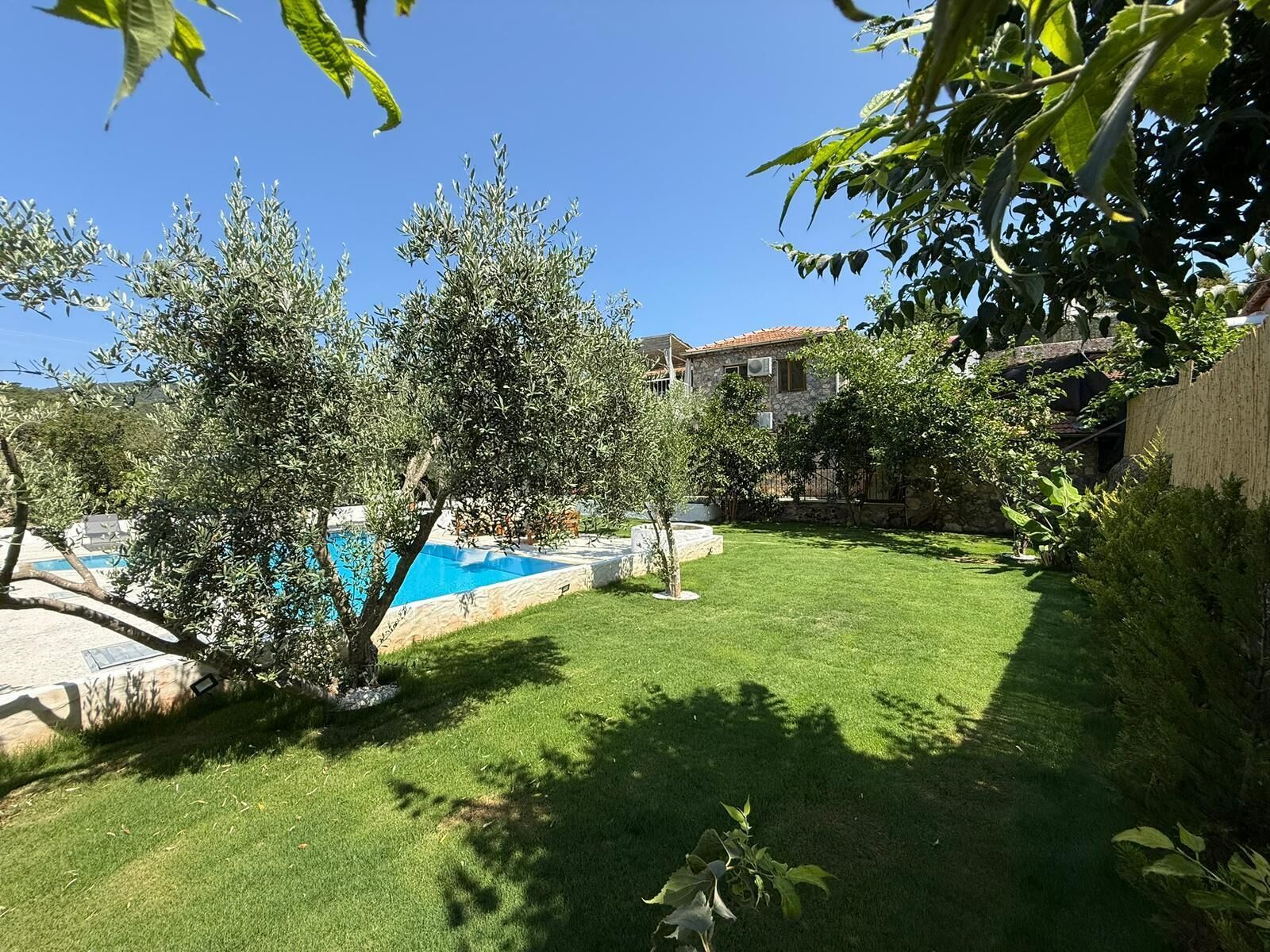 Un jardin avec une piscine, une maison en pierre et une pelouse bien entretenue.