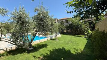 Un jardin avec une piscine, une maison en pierre et une pelouse bien entretenue.