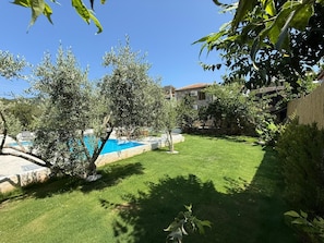 Un patio trasero con piscina, una casa de piedra y un césped bien cuidado.
