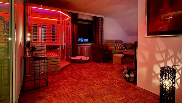 A room with a wooden parquet floor, a television, a sofa, a small table, and a decorative lantern. - Eifelsuiten First Floor - Das Nest (Wiesbaum)