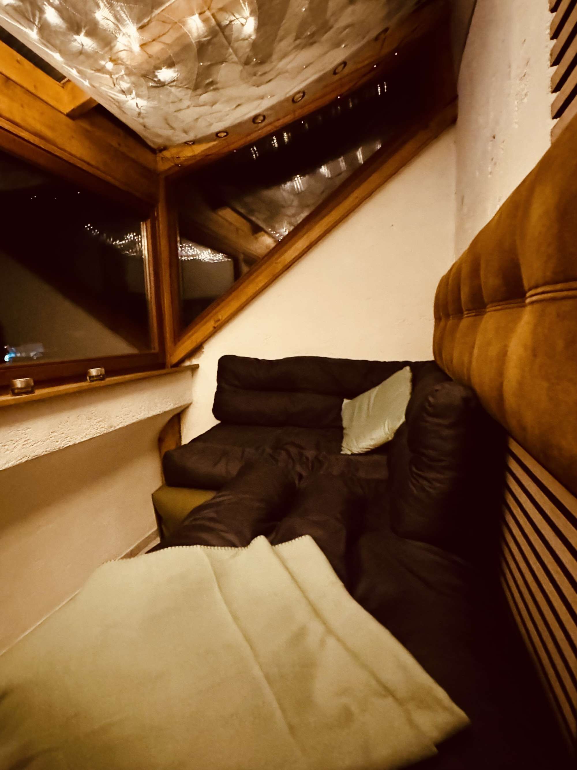 A room with a sloped ceiling, a window, a bed with pillows, and a wooden headboard.