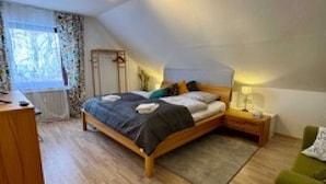 A bedroom with a bed, bedside tables, a green armchair, a wooden dresser, and a window with curtains. - Eifelsuiten First Floor - Das Nest (Wiesbaum)