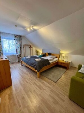A bedroom with a bed, bedside tables, a green armchair, a wooden dresser, and a window with curtains. - Eifelsuiten First Floor - Das Nest (Wiesbaum)