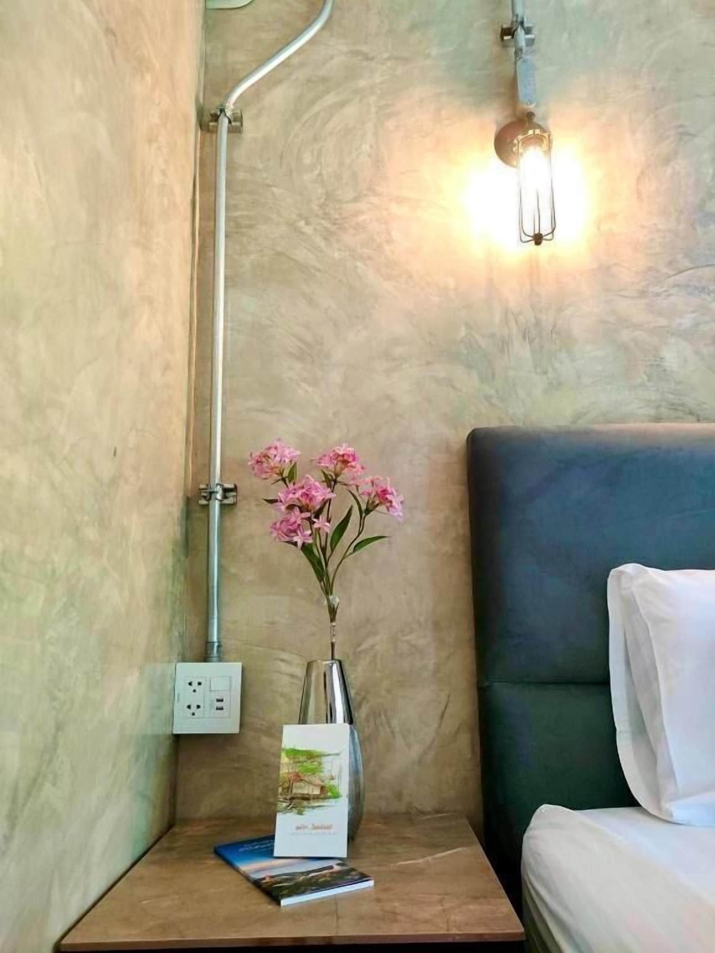 Un baño con ducha, una mesita de noche con un jarrón de flores, un libro y una lámpara de pared.