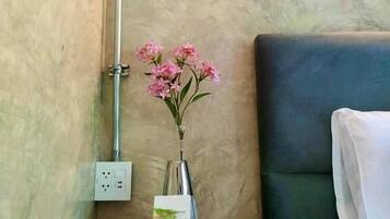 Un baño con ducha, una mesita de noche con un jarrón de flores, un libro y una lámpara de pared.