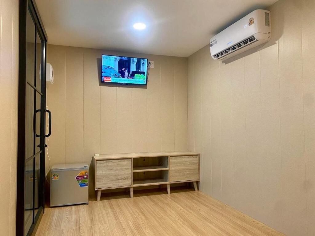 A room with a television mounted on the wall, a small cabinet, and an air conditioning unit.