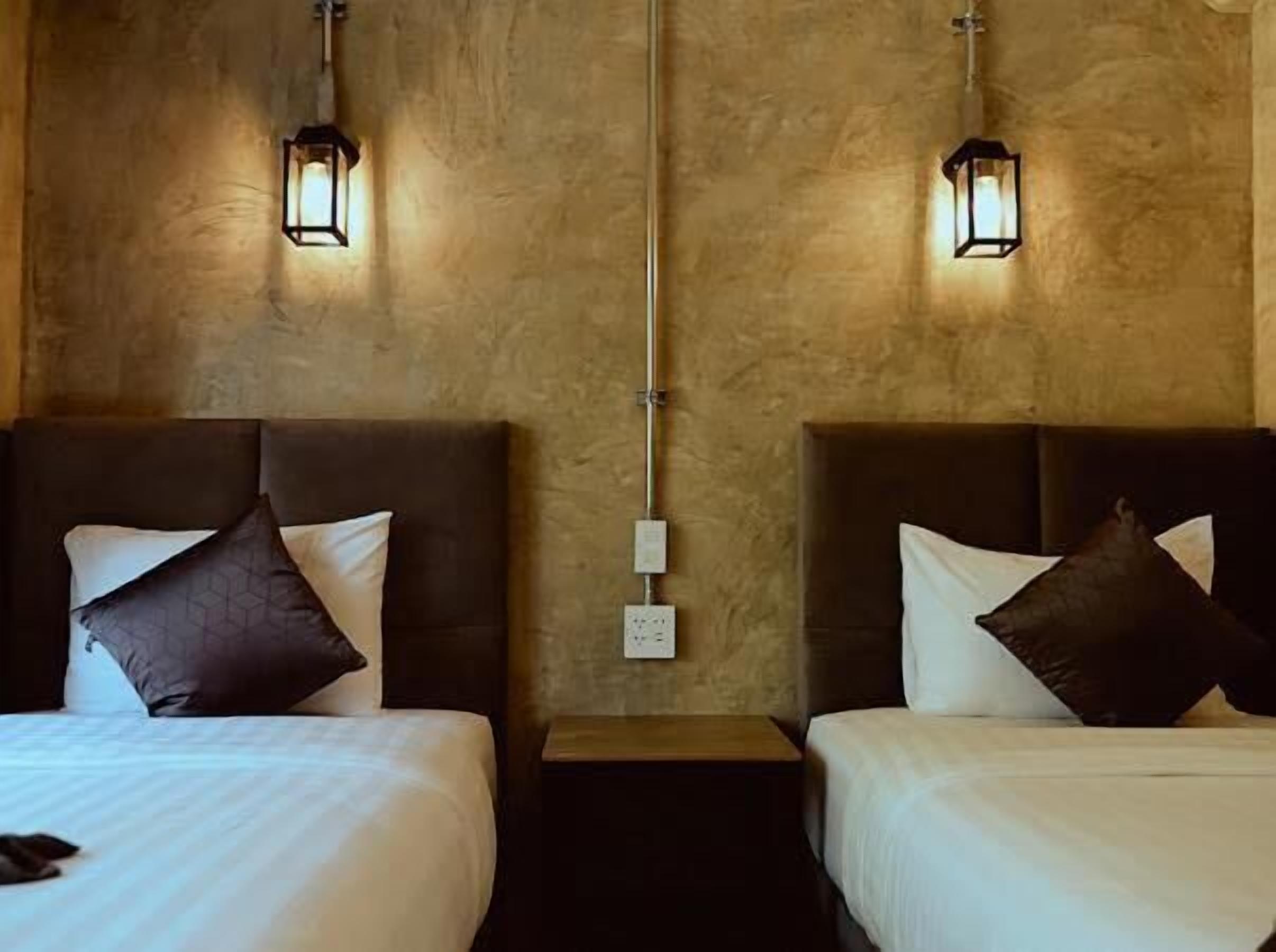 Habitación de hotel con dos camas, cada una con cabecero, mesita de noche y lámpara de pared.