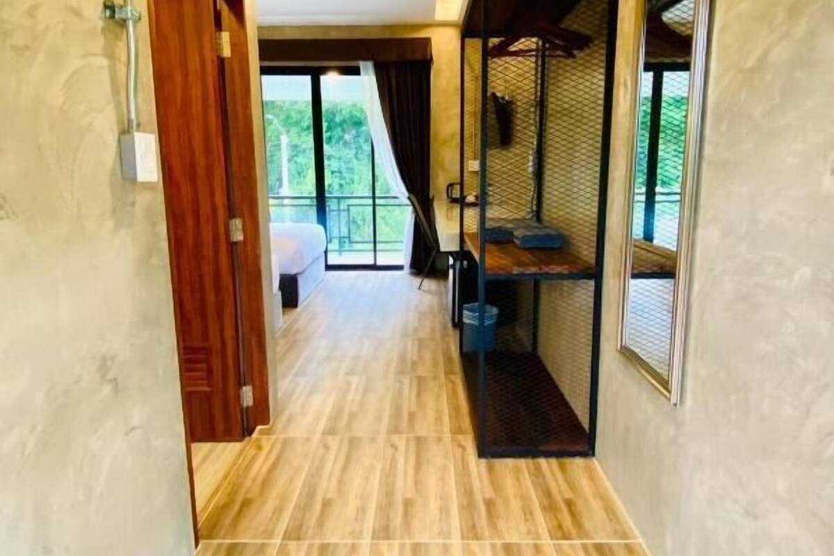 A hallway with wooden flooring, a bed in the background, and a window with a view.