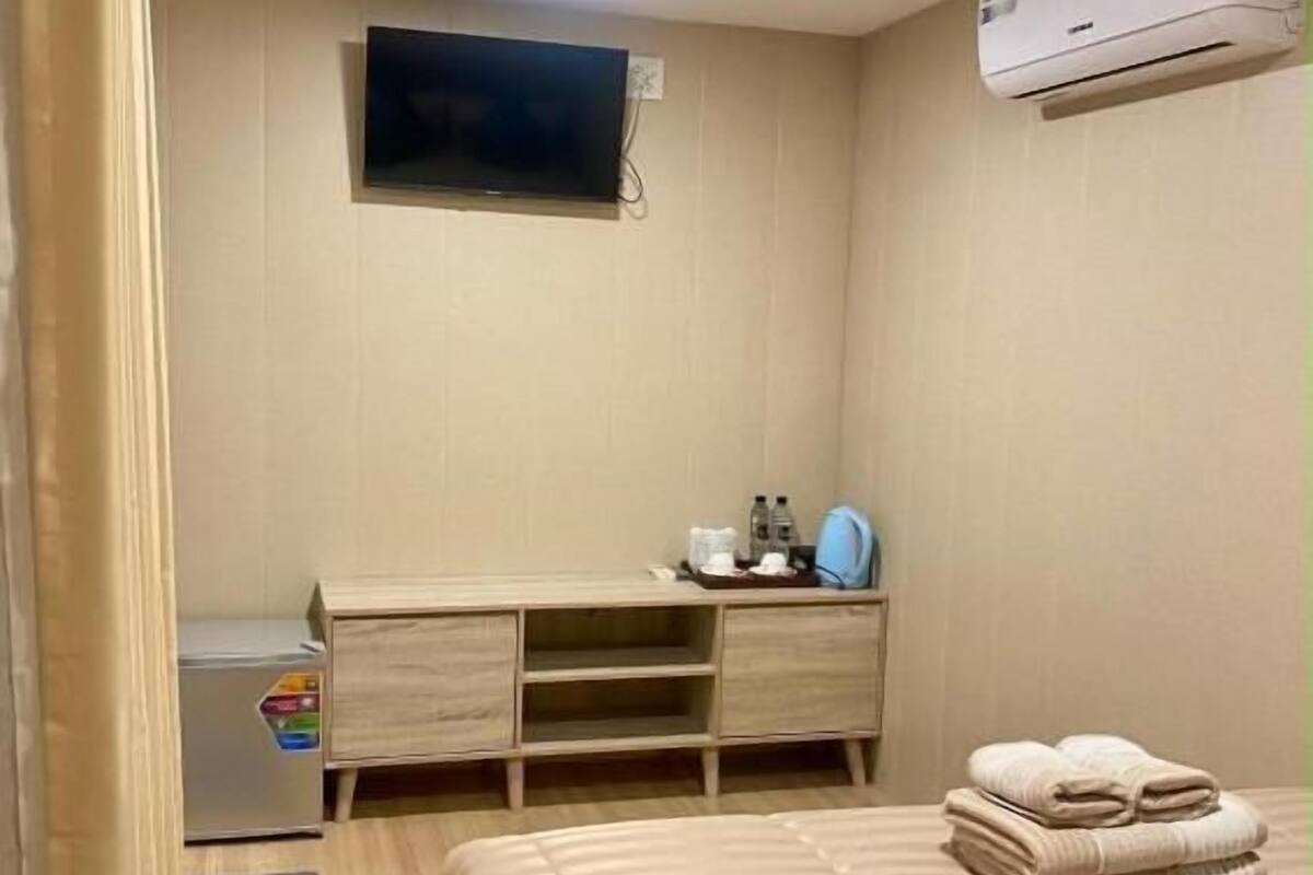 A hotel room with a bed, a TV mounted on the wall, a desk with a mirror, and an air conditioner.