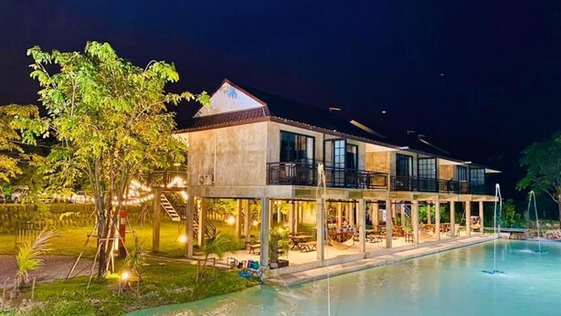 Um hotel de dois andares com piscina, área de estar ao ar livre e uma árvore.