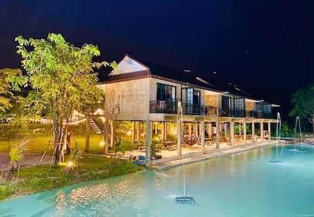 A two-story hotel with a swimming pool, outdoor seating, and a tree.. Tree House HomeStay