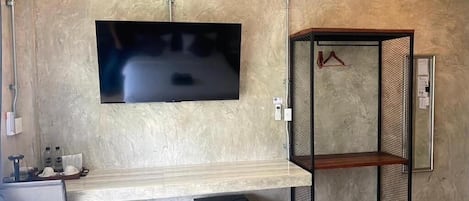 A room with a flat-screen TV mounted on the wall, a wooden bench, a metal shelving unit, and a trash bin.