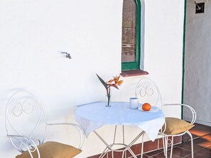 A small outdoor table with a white tablecloth, two metal chairs, a vase with flowers, and a plate with an orange. - Finca Luz de Palmera by Interhome (Santa Lucia de Tirajana)