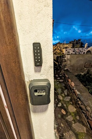 Una porta amb un teclat de parell encastat a la paret i un petit dispositiu rectangular, possiblement un sistema de seguretat, al costat d'una paret de pedra.