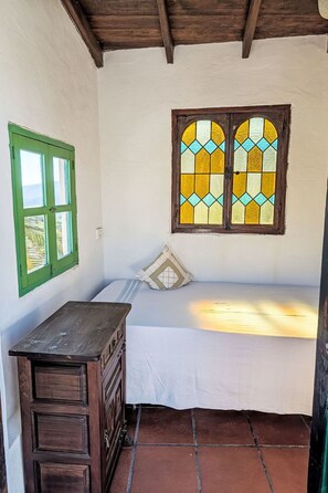 A room with a bed, a wooden desk, a green-framed window, and a stained glass window. - Finca Luz de Palmera by Interhome (Santa Lucia de Tirajana)