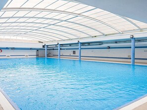 An indoor swimming pool with a curved glass ceiling, clear water, and blue poolside tiles. - Oceanview First Line with 2 Pools 6 by Interhome (Ovar / Praia de Esmoriz)