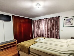 A bedroom with a bed, a wooden bench, a wardrobe, patterned curtains, and a framed picture on the wall. - Oceanview First Line with 2 Pools 6 by Interhome (Ovar / Praia de Esmoriz)