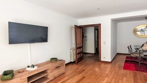 Uma sala de estar moderna com televisão de tela plana, móvel de entretenimento de madeira e área de jantar com tapete vermelho.