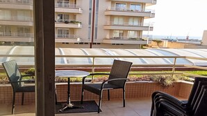 Uma varanda com mesa e cadeiras, dando para uma área residencial com edifícios altos e vista clara do mar.