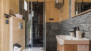 Un baño moderno con ducha, inodoro y lavamanos, con paredes de madera y una pared decorativa de piedra.