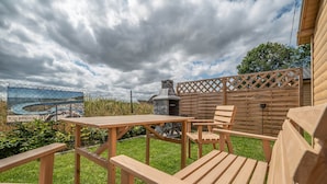 Una terraza de madera con una mesa, sillas, una parrilla metálica y una cerca de madera.