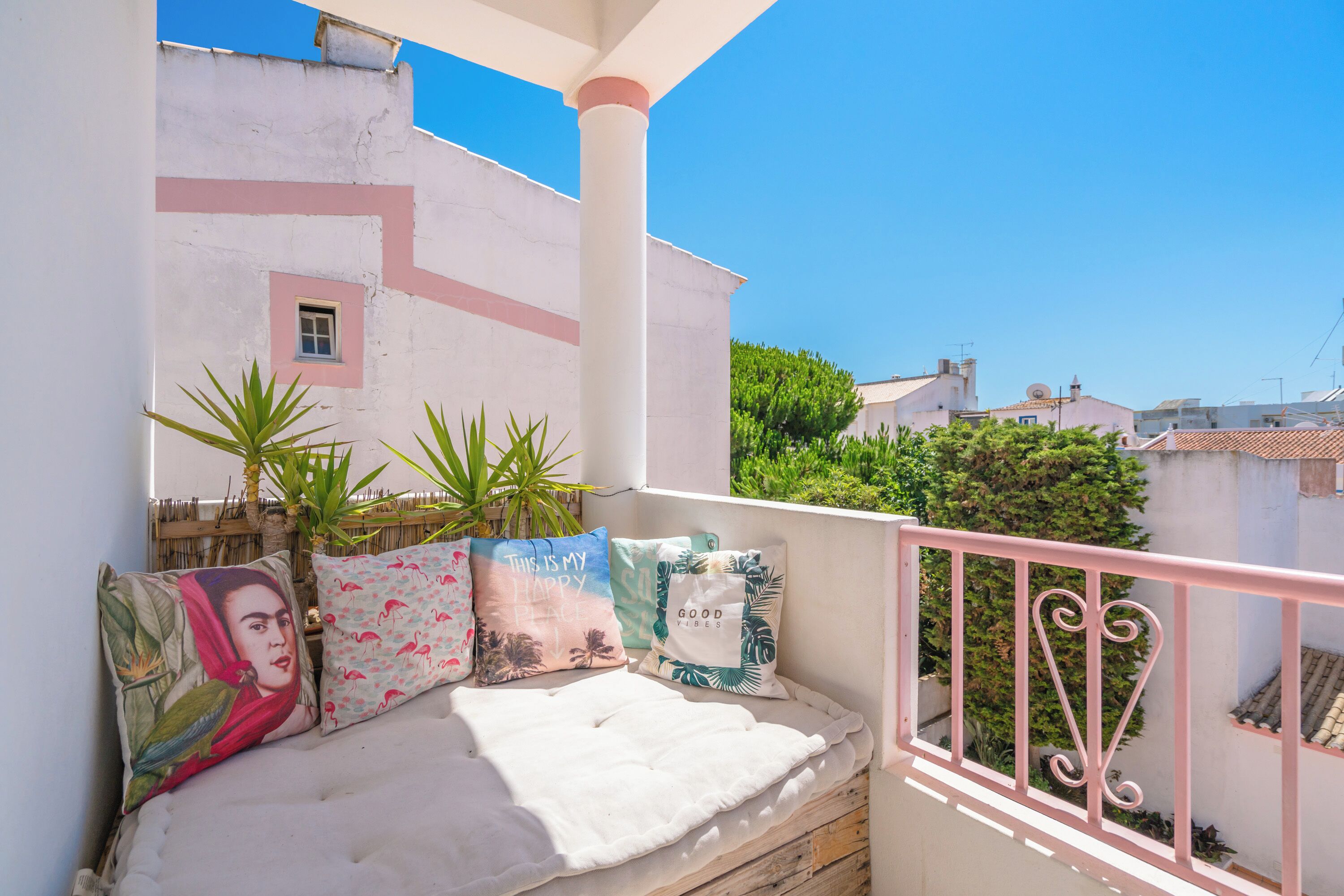 A balcony with a white cushioned bench, decorative pillows, and a pink railing.