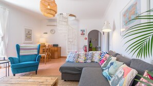 Una sala de estar con un sillón azul, sofá gris, mesa de centro de madera y una escalera.
