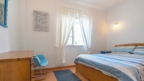 Un dormitorio con cama, escritorio, silla, ventana con cortinas y una pared con un cartel.