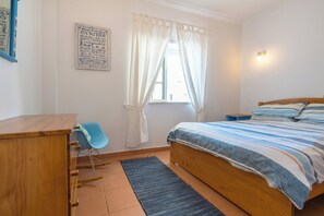 Ein Schlafzimmer mit Bett, Schreibtisch, Stuhl, einem Fenster mit Vorhängen und einem Wandzeichen.