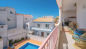 Un balcón con piscina, edificios blancos y mobiliario de mimbre.