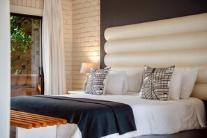A bed with white bedding and black and white patterned pillows, a wooden headboard, and a window with curtains. - Interlaken Guest House (Wilderness)