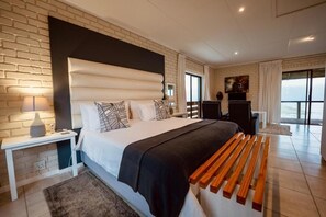 Ein modernes Schlafzimmer mit einem großen Bett, einem Nachttisch, einem Schreibtisch und Meerblick.