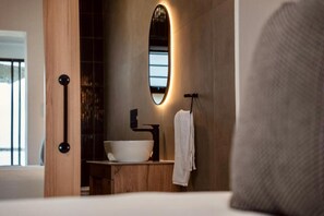 Ein modernes Badezimmer mit einem großen, ovalen Spiegel, einem weißen Waschbecken und einem Handtuchhalter.